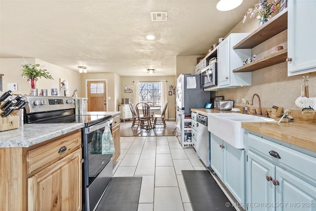 kitchen with light tile patterned floors, open shelves, light countertops, visible vents, and appliances with stainless steel finishes