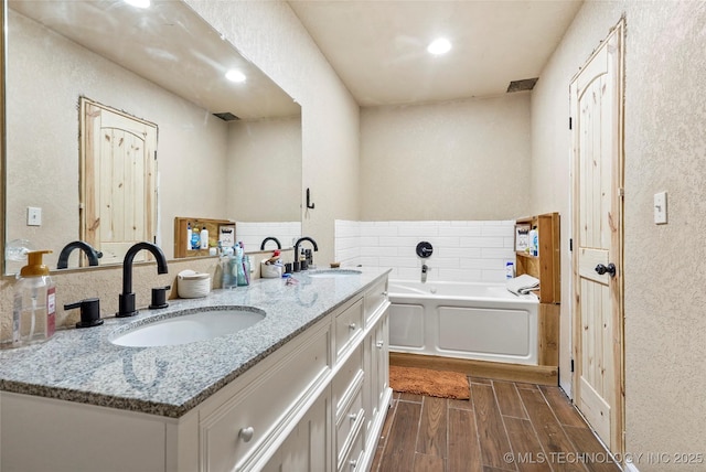 bathroom with wood tiled floor, a sink, a bath, and double vanity