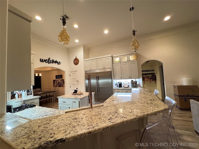 kitchen featuring arched walkways, stainless steel built in refrigerator, visible vents, and a kitchen island