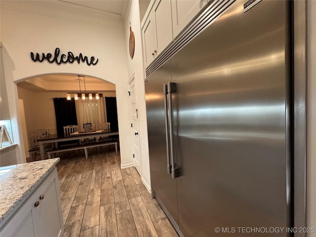 kitchen with arched walkways, white cabinets, stainless steel built in fridge, crown molding, and wood finish floors