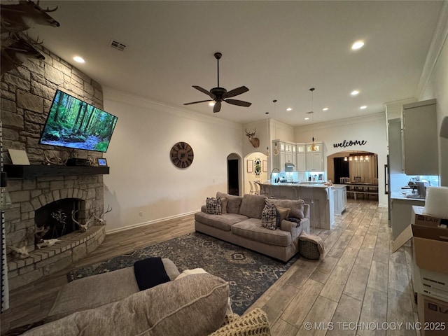 living room with arched walkways, light wood-style flooring, a fireplace, a ceiling fan, and crown molding