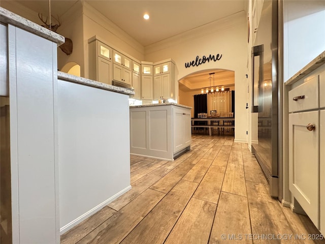 kitchen featuring light stone countertops, wood tiled floor, arched walkways, and ornamental molding