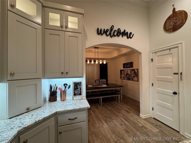 kitchen featuring arched walkways, ornamental molding, light stone countertops, a tray ceiling, and dark wood finished floors