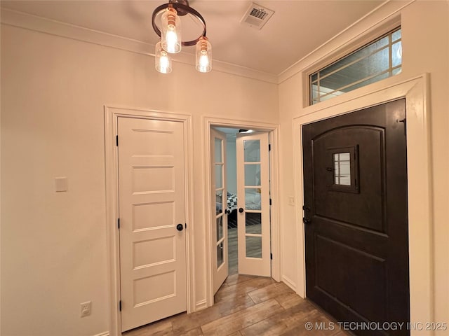 foyer entrance featuring baseboards, wood finished floors, visible vents, and crown molding