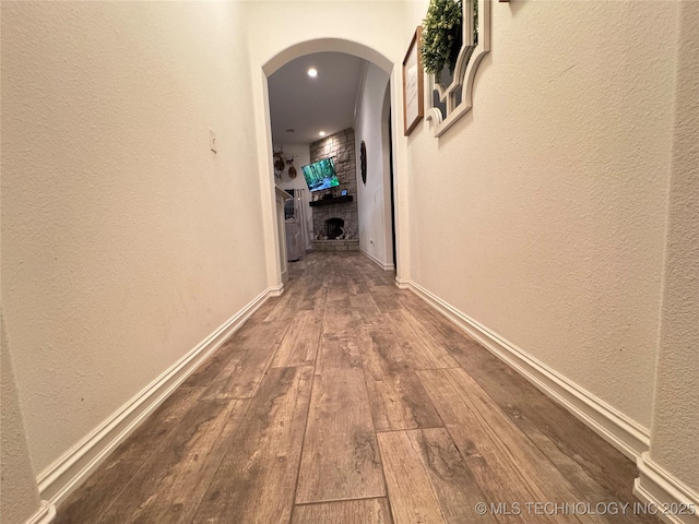 hall featuring arched walkways, wood-type flooring, a textured wall, and baseboards