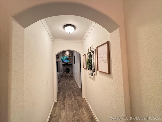 hallway with dark wood-style floors, arched walkways, ornamental molding, and baseboards