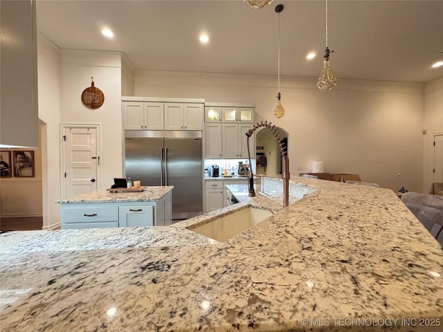 kitchen with a kitchen island, glass insert cabinets, light stone counters, crown molding, and built in fridge