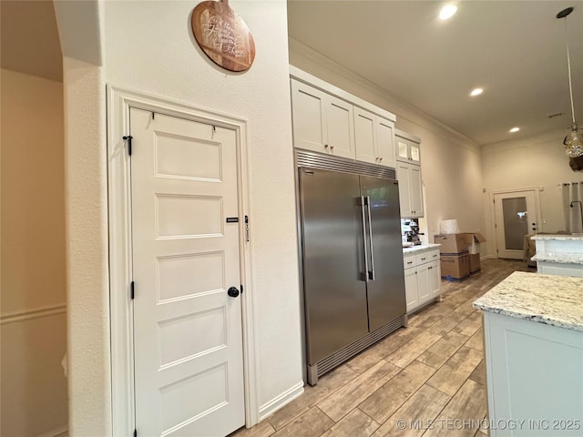 kitchen with light stone counters, recessed lighting, wood tiled floor, white cabinetry, and built in refrigerator