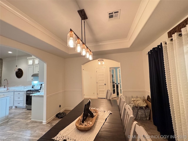 dining area with ornamental molding, arched walkways, a raised ceiling, and visible vents