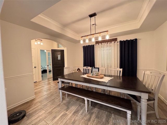 dining room featuring arched walkways, a tray ceiling, wood finished floors, and ornamental molding