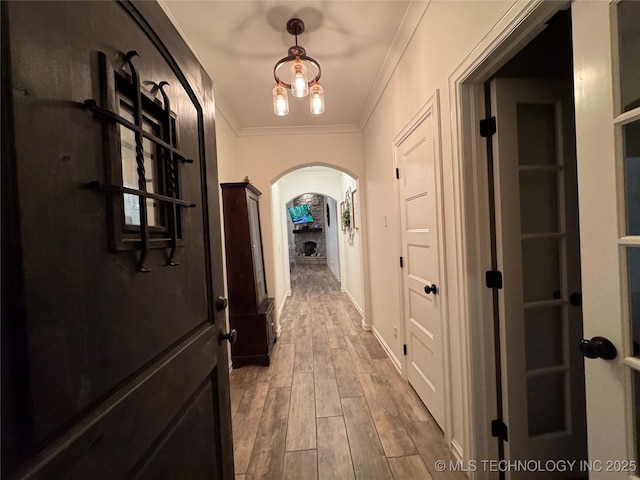 hall with arched walkways, wood finished floors, and ornamental molding