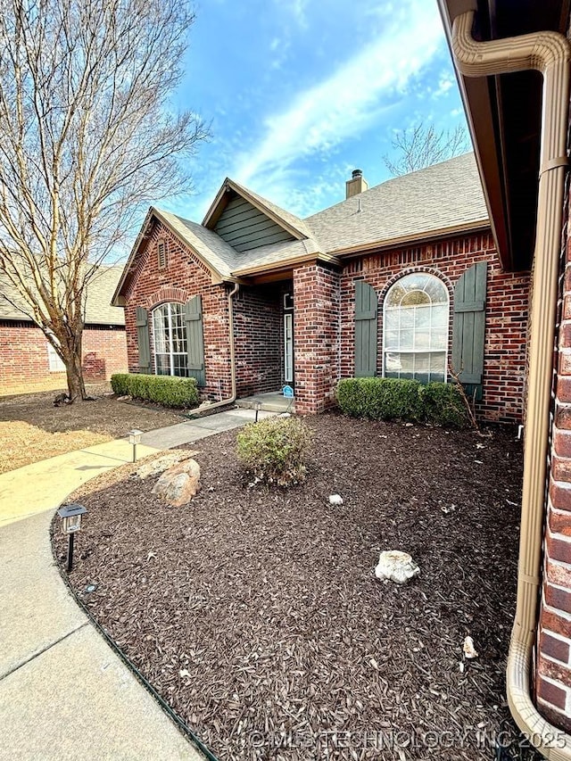 ranch-style home with roof with shingles, a chimney, and brick siding