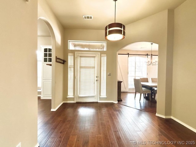 foyer featuring arched walkways, a barn door, and dark wood-style flooring