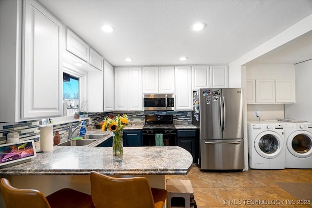 kitchen with a breakfast bar, a sink, white cabinets, washer and dryer, and appliances with stainless steel finishes