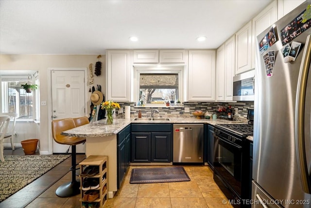 kitchen with tasteful backsplash, appliances with stainless steel finishes, a peninsula, white cabinetry, and a sink