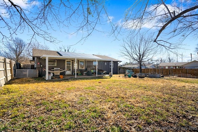 back of house with a lawn, solar panels, a patio, a fenced backyard, and board and batten siding