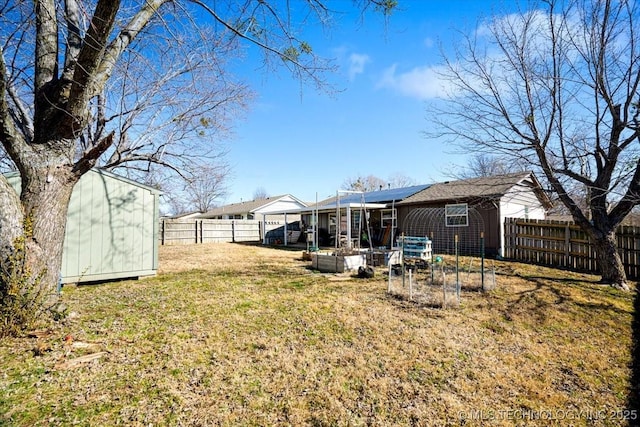 back of property with a fenced backyard, an outdoor structure, a garden, roof mounted solar panels, and a shed