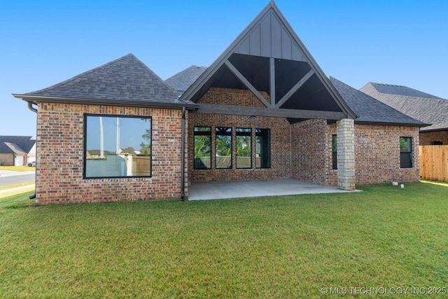 back of house featuring a patio area, roof with shingles, a lawn, and brick siding