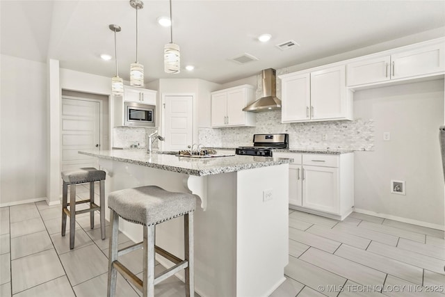 kitchen with visible vents, wall chimney exhaust hood, appliances with stainless steel finishes, white cabinetry, and backsplash