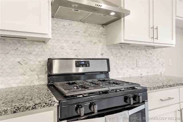 kitchen featuring decorative backsplash, white cabinetry, light stone countertops, under cabinet range hood, and gas range