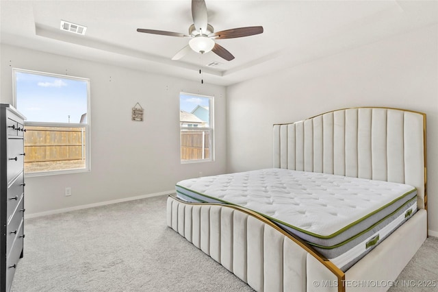 bedroom with carpet floors, a tray ceiling, visible vents, and baseboards