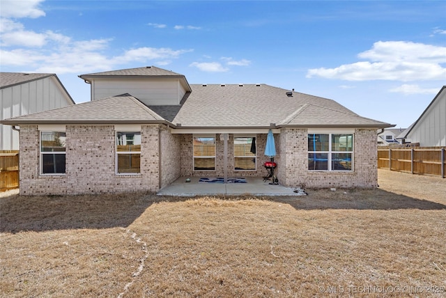 rear view of property featuring a patio area, fence, brick siding, and roof with shingles