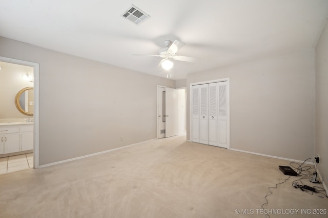 unfurnished bedroom featuring a closet, visible vents, ensuite bathroom, light carpet, and baseboards