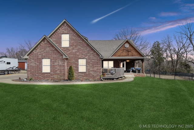 back of property at dusk featuring a shingled roof, fence, a lawn, and brick siding