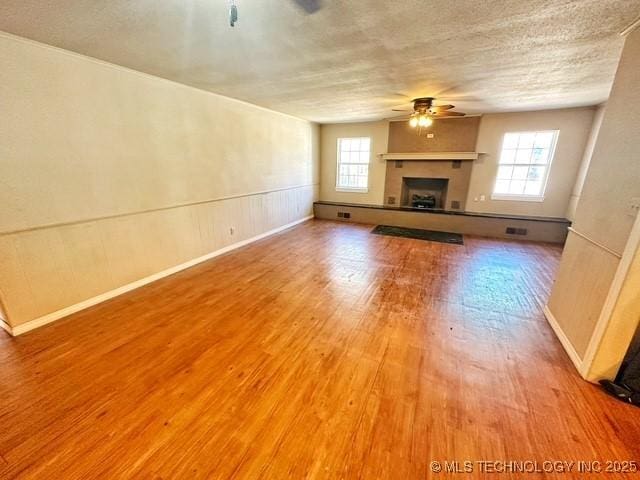 unfurnished living room with a healthy amount of sunlight, ceiling fan, a fireplace with raised hearth, and wood finished floors