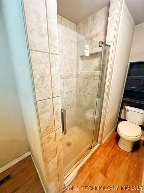 full bath featuring a stall shower, baseboards, toilet, and wood finished floors