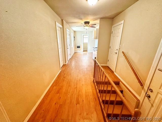 corridor featuring an upstairs landing, light wood-style flooring, and baseboards