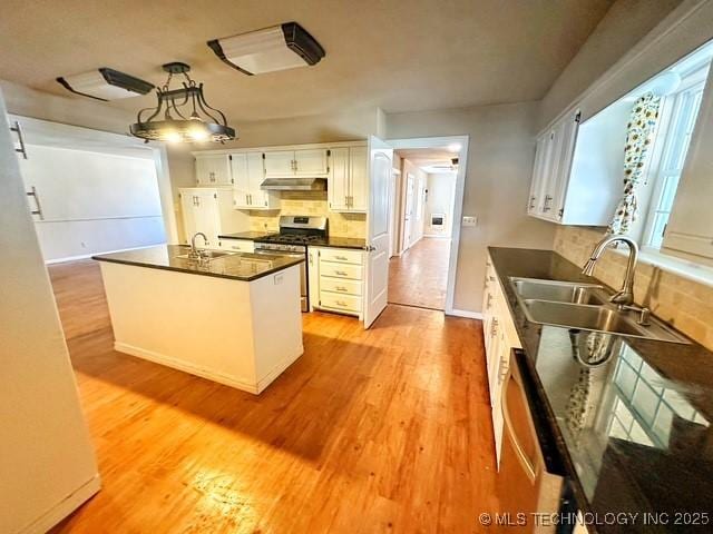 kitchen featuring light wood finished floors, dark countertops, appliances with stainless steel finishes, white cabinets, and a sink