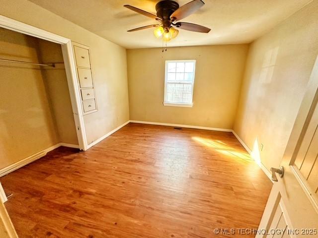 unfurnished bedroom featuring a closet, wood finished floors, a ceiling fan, and baseboards