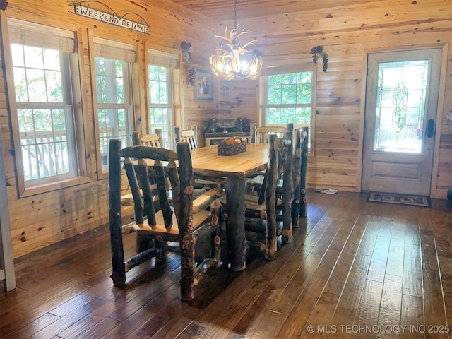 dining area with dark wood-style flooring, wooden walls, and an inviting chandelier