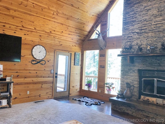 unfurnished living room featuring a fireplace, visible vents, wood walls, high vaulted ceiling, and wooden ceiling