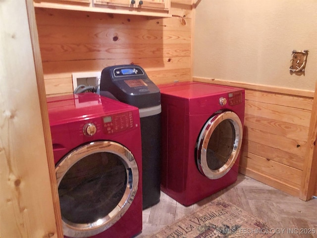 laundry room with laundry area, a wainscoted wall, wooden walls, and washing machine and clothes dryer