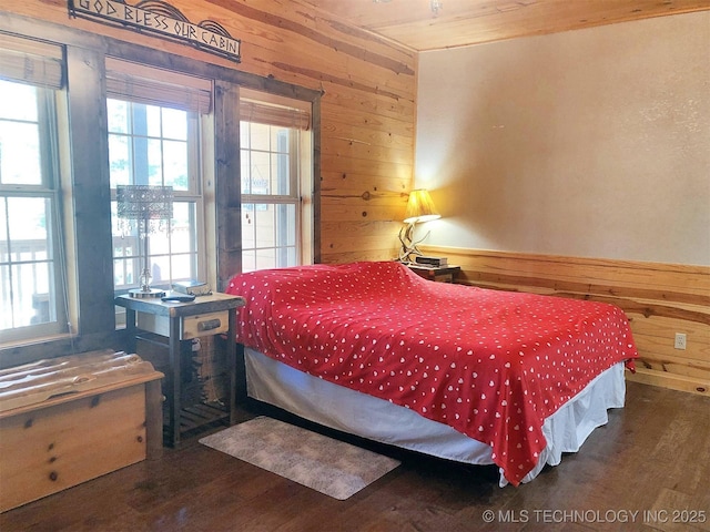 bedroom with multiple windows, wooden walls, and wood finished floors