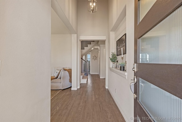 foyer entrance featuring baseboards, a towering ceiling, wood finished floors, stairs, and a chandelier