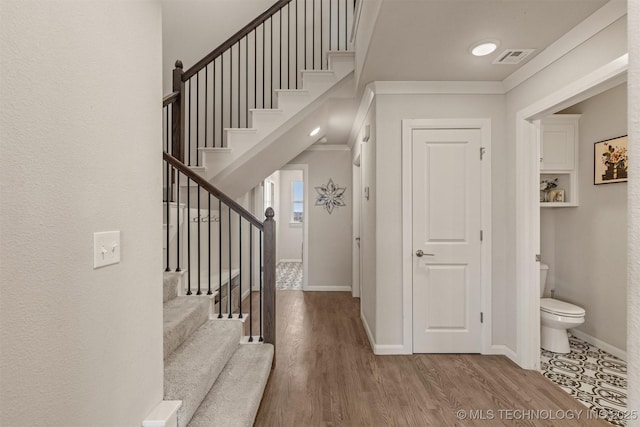 foyer entrance featuring baseboards, wood finished floors, visible vents, and crown molding