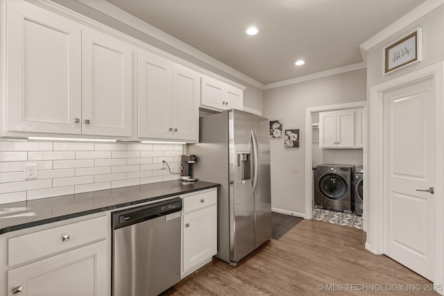 kitchen featuring crown molding, dark countertops, appliances with stainless steel finishes, washing machine and dryer, and white cabinets