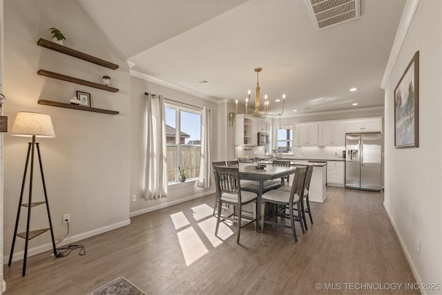 dining space featuring visible vents, crown molding, baseboards, and wood finished floors