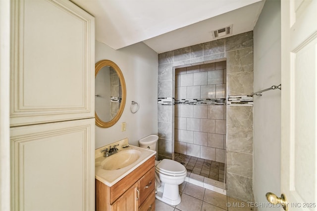 bathroom with tile patterned flooring, toilet, vanity, visible vents, and a tile shower