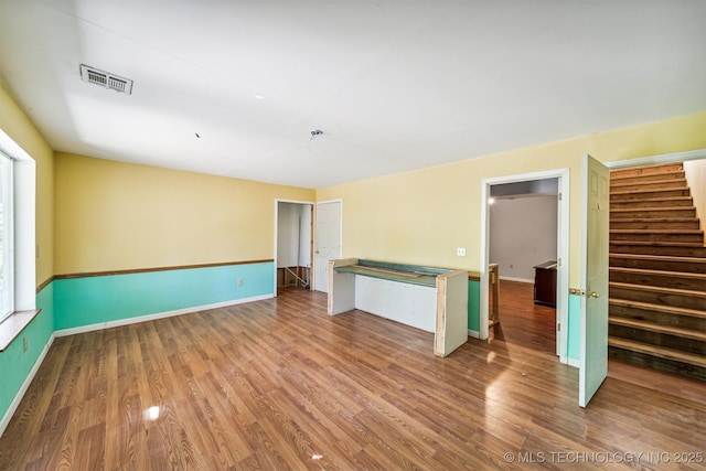 spare room with visible vents, stairway, baseboards, and wood finished floors