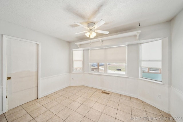 empty room with light tile patterned floors, a textured ceiling, visible vents, and a ceiling fan