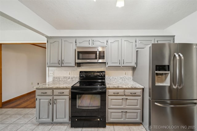 kitchen featuring light tile patterned floors, gray cabinetry, appliances with stainless steel finishes, decorative backsplash, and light stone countertops