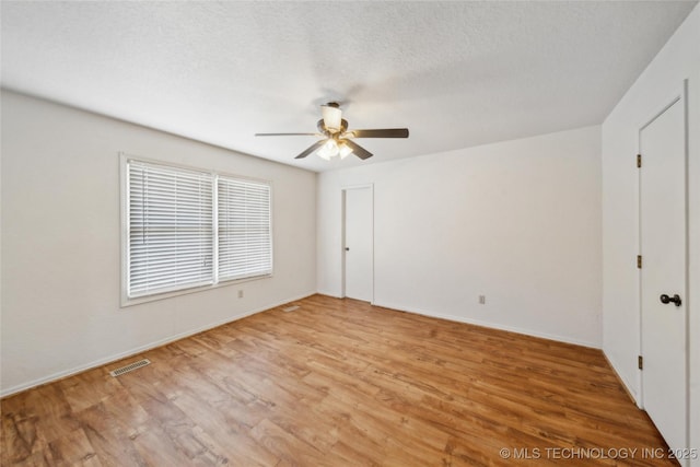 unfurnished bedroom featuring a textured ceiling, light wood-style flooring, visible vents, baseboards, and a ceiling fan