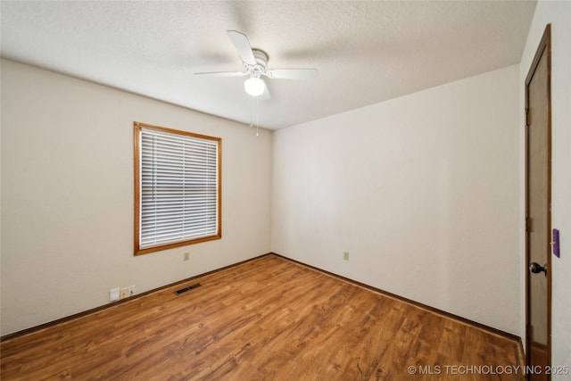 empty room with a ceiling fan, a textured ceiling, visible vents, and wood finished floors