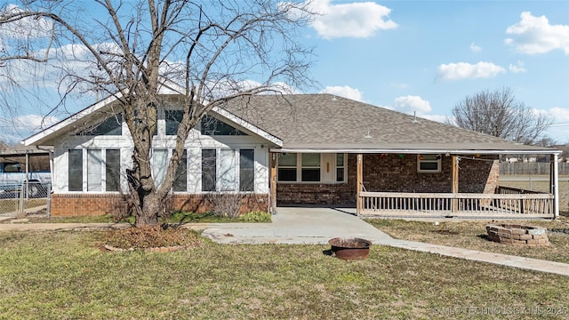 view of front facade with an outdoor fire pit, brick siding, a shingled roof, fence, and a front lawn