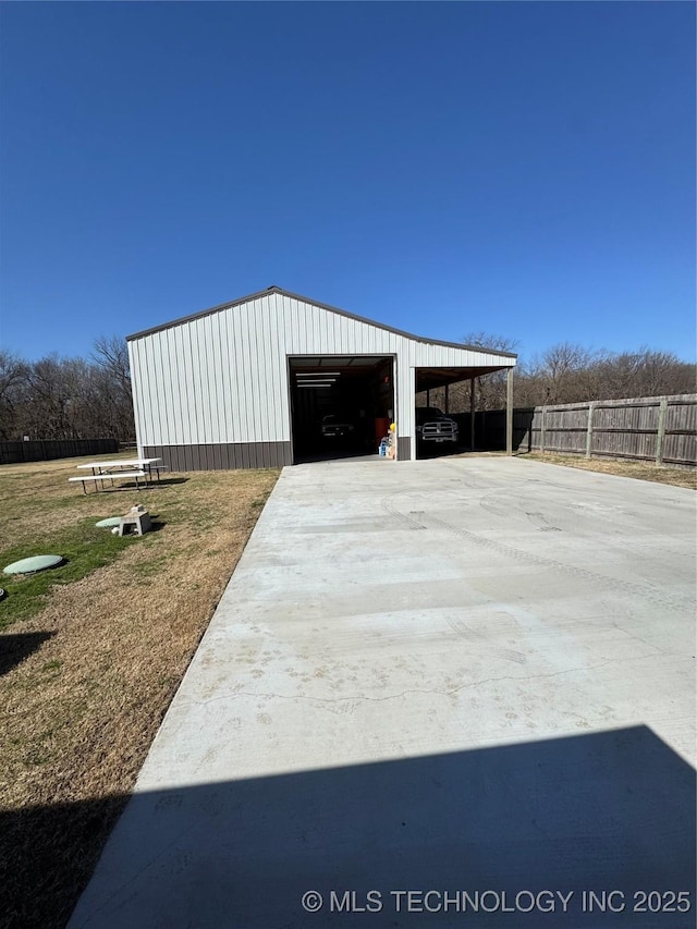 view of outdoor structure featuring fence, concrete driveway, and an outbuilding