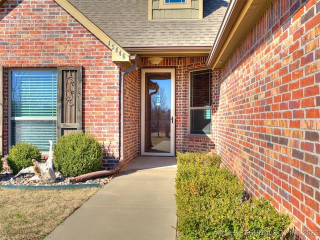 view of exterior entry with brick siding and a shingled roof